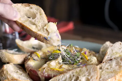 Une personne trempe des tranches de pain camembert fondu